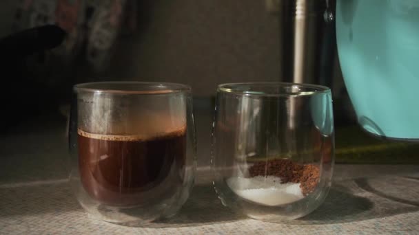 Küche, auf der Arbeitsplatte, kochendes Wasser aus der blauen Teekanne in zwei doppelbödige Gläser mit Instant-Kaffee, Zucker gegossen. Morgens fallen helle Sonnenstrahlen aus dem Fenster. Glasschirm, Dampf. Statisch - Filmmaterial, Video