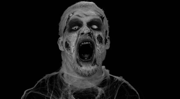 Nieoczekiwane pojawienie się przerażającego człowieka z krwawym zombie Halloween, zranionym makijażem, próbującego wystraszyć, wyraz twarzy. Temat horroru. Złowrogi nieumarły facet odizolowany na czarnym tle studia - Zdjęcie, obraz