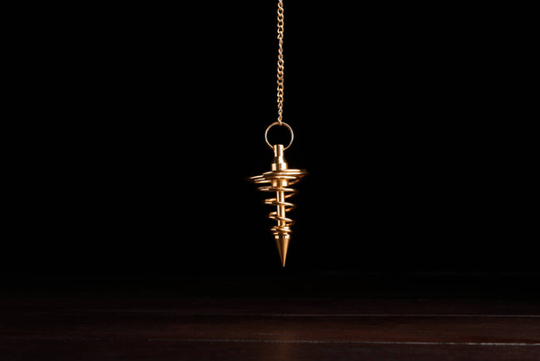 Stylish pendulum above wooden table on black background. Hypnotherapy session - Фото, зображення
