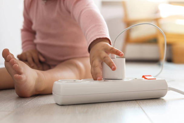 Cute baby playing with charger and power strip on floor at home, closeup. Dangerous situation - Фото, зображення