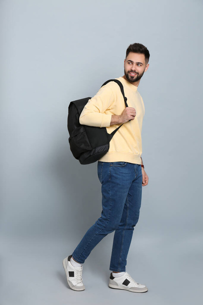Young man with stylish backpack walking on light grey background - Photo, Image