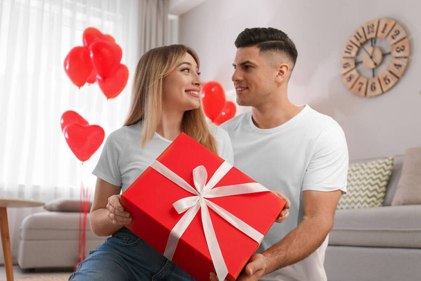 Man presenting gift to his girlfriend in room decorated with heart shaped balloons. Valentine's day celebration - Zdjęcie, obraz