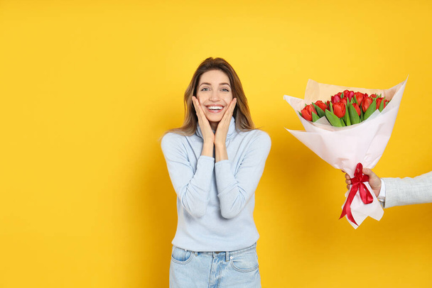Happy woman receiving red tulip bouquet from man on yellow background. 8th of March celebration - Foto, imagen
