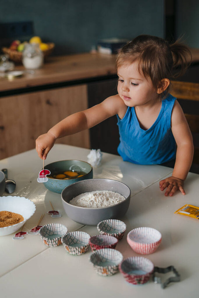 Kaukasisches Mädchen, das in der Küche sitzt und dabei hilft, Eier in Schalen zu schlagen. Neue Fähigkeiten, Kindheit, Mutterschaft. Glückliche Familie, Kind Tochter kocht Essen in - Foto, Bild