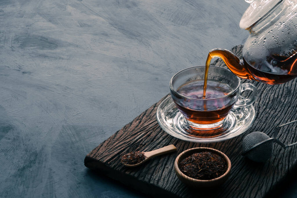 Process brewing tea, Hot tea water is poured from the teapot into a cup on the old wood plank with dark kitchen table background, still life relaxing time dark mood style. - 写真・画像