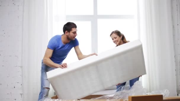 smiling couple opening big cardboard box with sofa - Кадри, відео