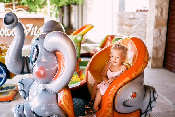 Little girl sits on an elephant-shaped carousel. High quality photo - Photo, Image