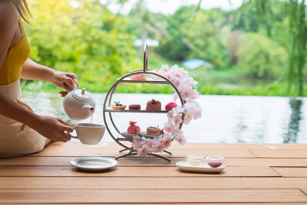 Nainen käsi kaatamalla kuumaa teetä Afternoon teepakkaus ja Pink jälkiruoka ylellisessä hotellissa - Valokuva, kuva