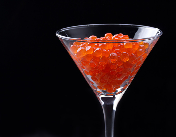 Red caviar in wineglass on black background - Фото, изображение