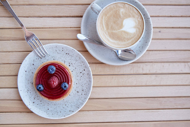 Ranskalainen tuore makea mustikka ja vadelma torttu valkoinen keraaminen levy kuppi cappuccino. Kahvin ja aamiaisen aika. Top näkymä ruoka - Valokuva, kuva