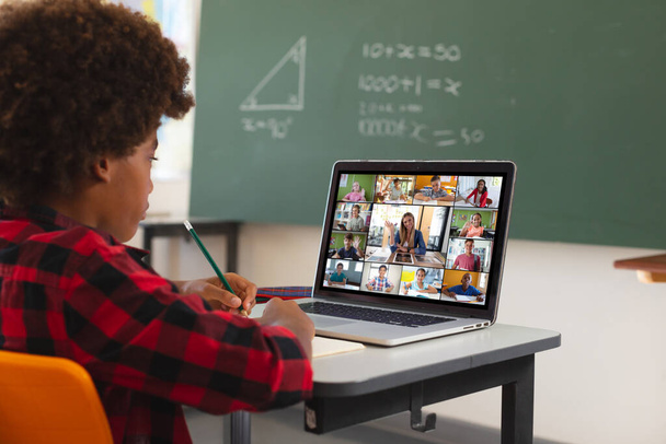 African american boy using laptop for video call, with diverse elementary school pupils on screen. communication technology and online education, digital composite image. - Photo, image