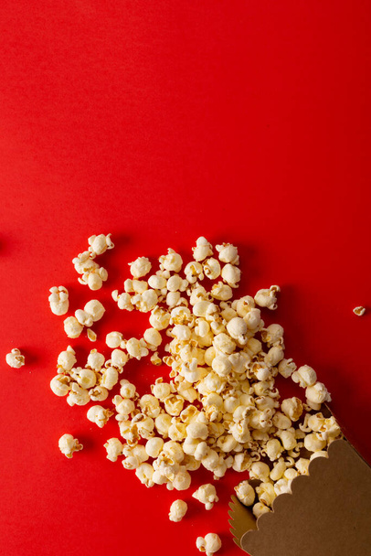 Vertical image of pop corn lying on red surface. Food, snacks, cinema and american cuisine concept. - Foto, Imagem