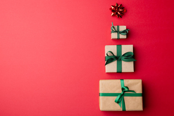 Εικόνα από χριστουγεννιάτικα δώρα που σχηματίζουν χριστουγεννιάτικο δέντρο και αντίγραφο χώρου σε κόκκινο φόντο. Χριστούγεννα, παράδοση και εορταστική έννοια. - Φωτογραφία, εικόνα