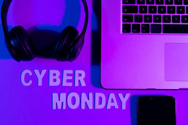 Image of cyber monday text, smartphone, laptop and headphones over neon purple background. Retail, savings, online shopping, light and colour concept. - Foto, Imagen