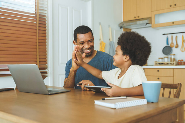 Happy Black African American father and son giving high five while using laptop and digital tablet. - Fotó, kép