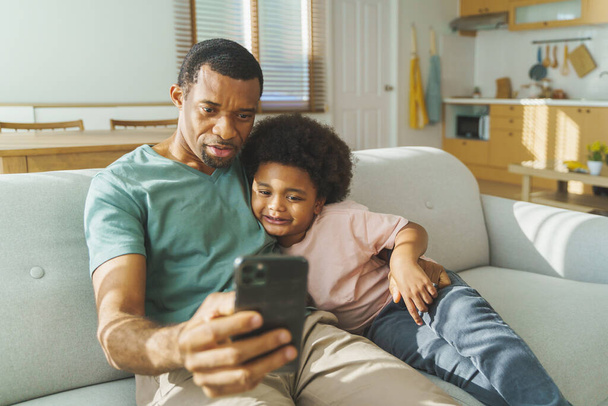 Black African American father and son using smartphone at home. Happy smiling African Man and little child having video call - Valokuva, kuva