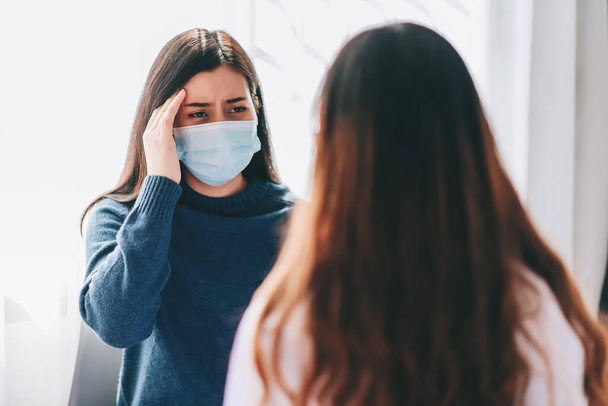 Aziatische arts bezoek en onderzoekt op jonge volwassen vrouw in het ziekenhuis met hoofdpijn. De arts controleert en adviseert voor de gezondheidszorg, draagt een masker ter bescherming van covid-19 pandemie. - Foto, afbeelding
