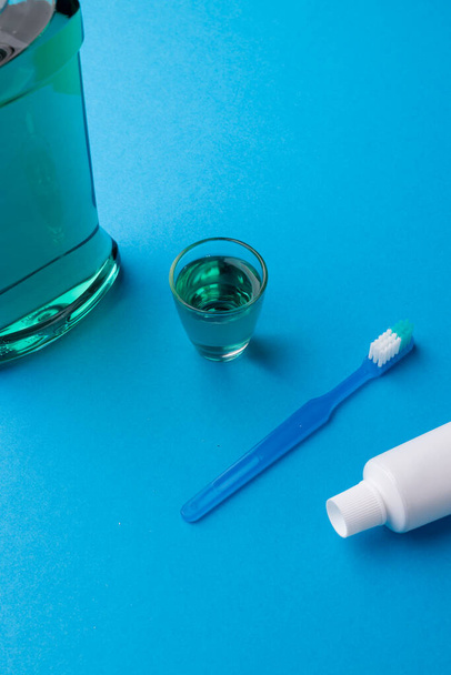 Vertical image of cleaning liquid, toothbrush and toothpaste on blue surface. Health, dentistry, dental accessories and taking care of teeth concept. - Photo, image
