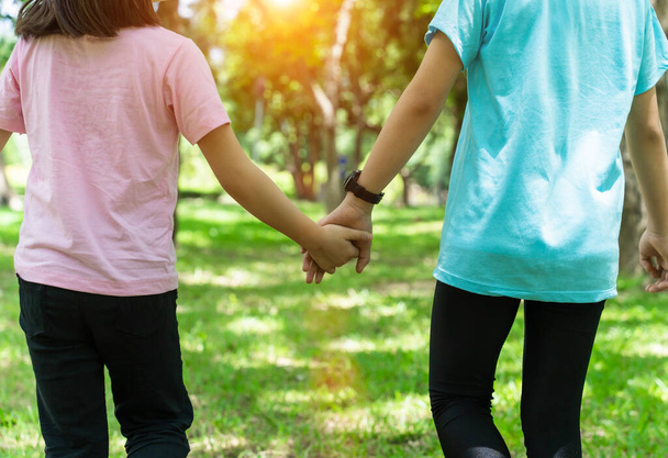 Two sister holding hands in the park in warm spring day. Happy friendship family concept. - Fotoğraf, Görsel