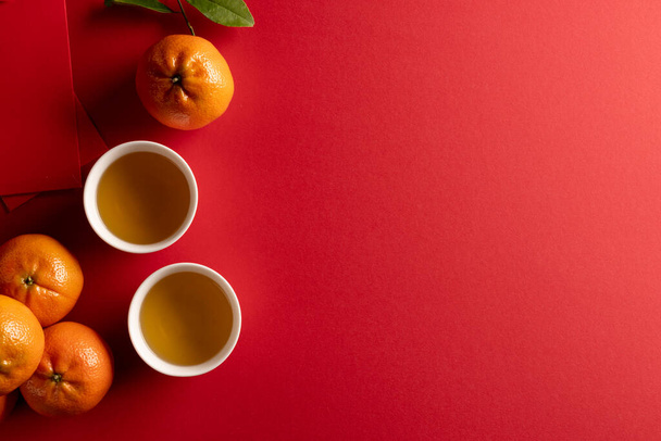 Composition of traditional chinese decorations and oranges on red background. Chinese new year, tradition and celebration concept. - Foto, immagini