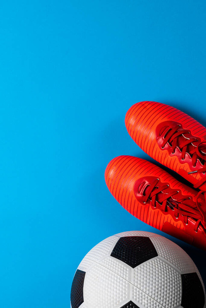 Composition of football and red shoes on blue background with copy space. Sport, movement, training and active lifestyle concept. - Photo, Image