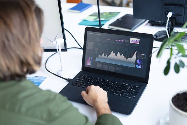 Caucasian businesswoman sitting at desk, using laptop with statistical data on screen. business communication and digital interface technology digital composite image. - Valokuva, kuva