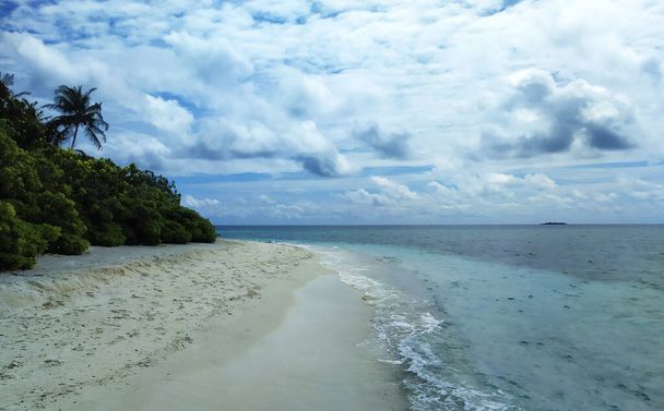 Maldives, the deserted beach with white sand and trees near the blue ocean. Summer vacation on a tropical island. Luxury travel. Tranquility and relaxation. Sea horizon with a small island on it. - Foto, afbeelding