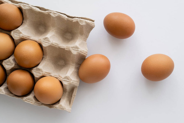 Top näkymä ruskeat munat lähellä pahvilaatikkoa valkoisella pohjalla  - Valokuva, kuva
