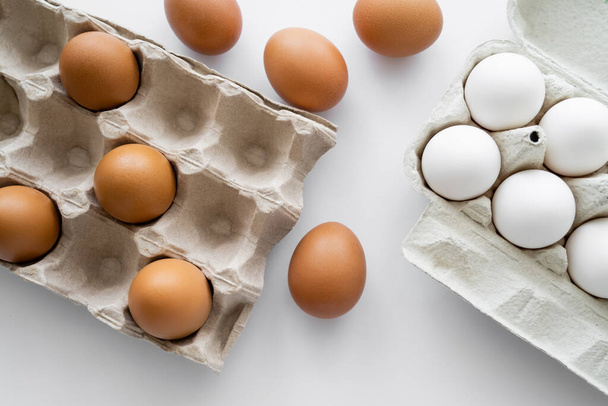 Top view of natural eggs and carton containers on white background  - Valokuva, kuva