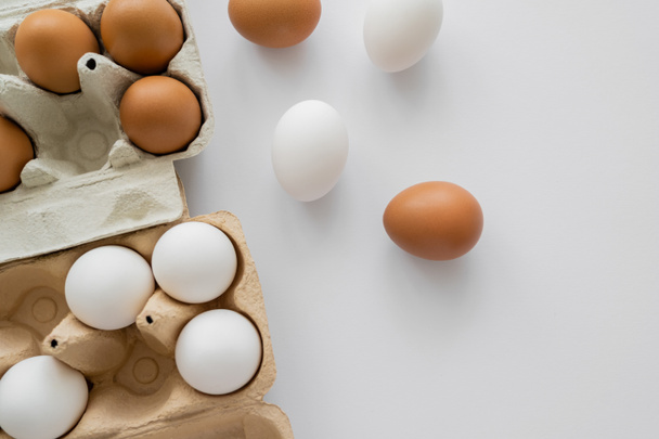 Vista superior de huevos en cáscaras cerca de cajas de cartón sobre fondo blanco  - Foto, imagen