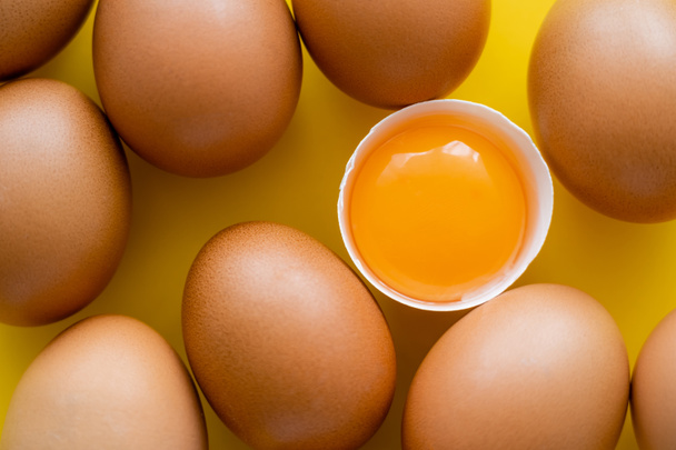 Close up view of fresh yolk in shell near eggs on yellow background  - Photo, Image
