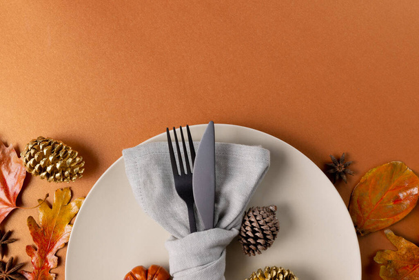 Overhead view of plate and cutlery with autumn decoration and copy space on orange background. Thanksgiving, autumn, fall, american tradition and celebration concept. - Foto, immagini