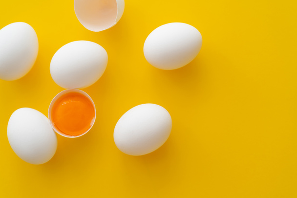 Top view of natural yolk in shell near eggs on yellow background  - Photo, image