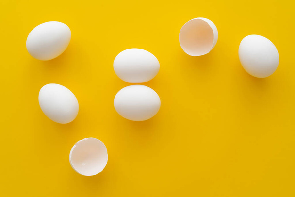 Vue du dessus des œufs blancs et des coquilles sur fond jaune  - Photo, image