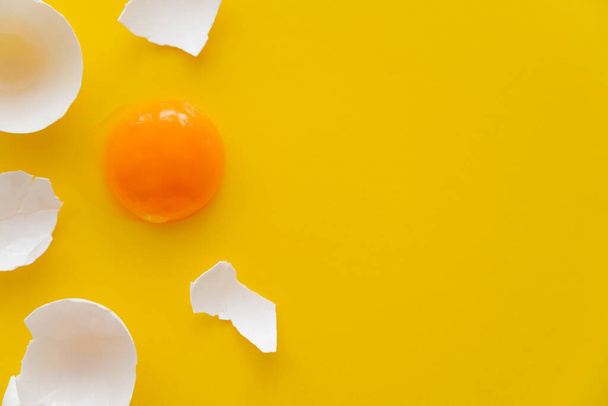 Top view of natural yolk and cracked egg shell on yellow background  - Foto, immagini