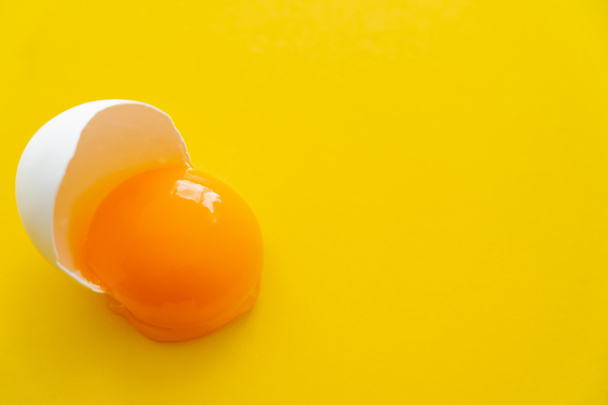 Zblízka pohled na syrový přírodní vaječný žloutek ve skořápce na žlutém pozadí  - Fotografie, Obrázek