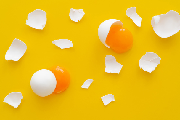 Top view of natural yolks and cracked egg shells on yellow background  - Photo, image