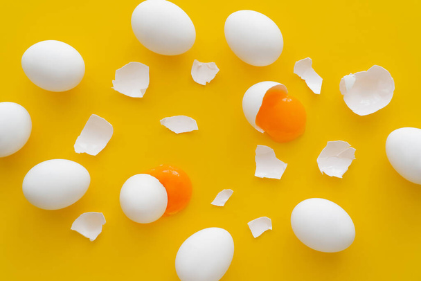 Top view of eggs near yolks and cracked shells on yellow background  - Фото, изображение