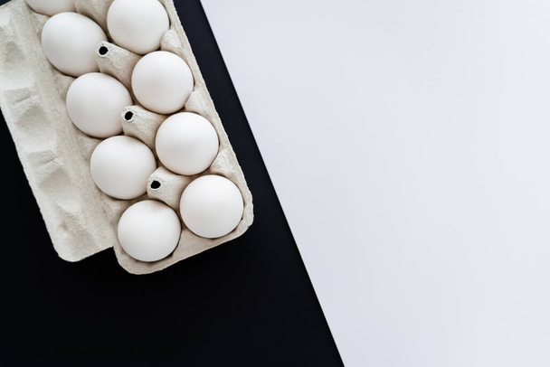 Horní pohled na přírodní kuřecí vejce v papírové vaničce na bílém a černém pozadí s kopírovacím prostorem  - Fotografie, Obrázek