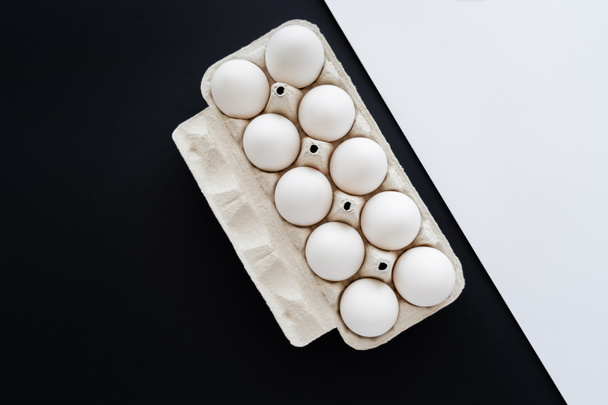 Vista dall'alto di uova di pollo fresche in vassoio su superficie bianca e nera  - Foto, immagini