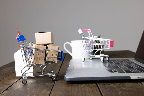 Composition of shopping carts with boxes and laptop on gray background. Retail, shopping and black friday concept. - Photo, Image
