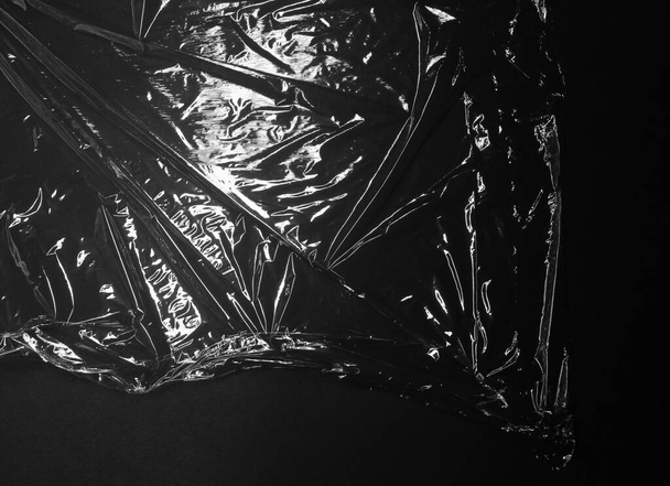 Reflecting light and shadow on creases and folds in clear plastic foil on black background. monochrome light and texture, abstract background image. - Foto, Imagem