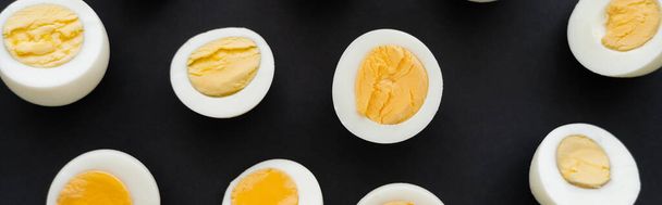 Top view of cut boiled eggs with yolks on black background, banner  - Foto, afbeelding
