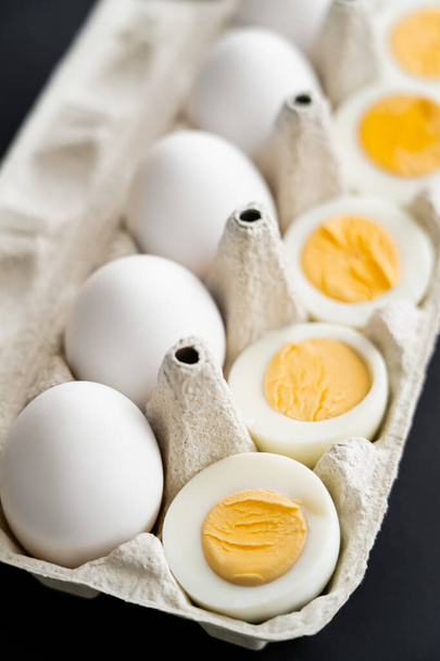 Close up view of cut boiled and raw eggs in blurred carton tray isolated on black  - Fotografie, Obrázek