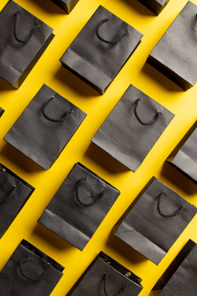 Composition of gray paper shopping bags on yellow background. Retail, shopping and black friday concept. - 写真・画像