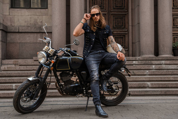 Снимок жестокого мотоциклиста с бородой и длинными волосами за рулем мотоцикла. - Фото, изображение