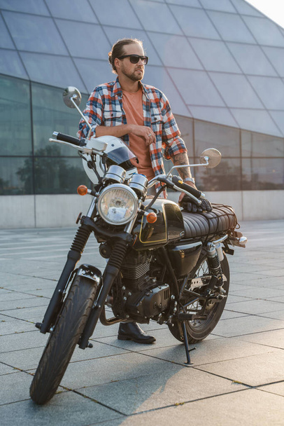 Портрет бородатого байкера в солнцезащитных очках и старомодном мотоцикле. - Фото, изображение