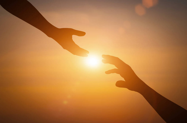 Silueta natahování, dává pomocnou ruku, naději a podporu navzájem během západu slunce pozadí. - Fotografie, Obrázek