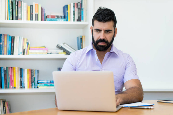Serious hispanic businessman with beard working at computer at desk at office - Φωτογραφία, εικόνα