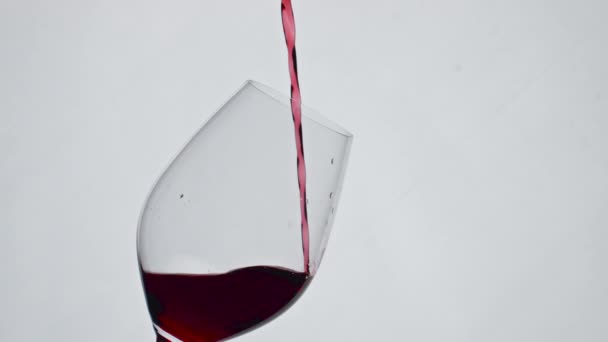 Nahaufnahme rote Flüssigkeitsfüllung Weinglas Super-Zeitlupe. Alkoholischer Wein, der in einem sauberen Becher plätschert. Erfrischendes Rosengetränk schenkt Glas weißen Hintergrund. Kippelkonzept für luxuriöse Eleganz  - Filmmaterial, Video